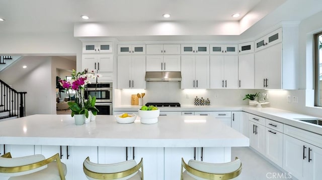 kitchen with under cabinet range hood, double oven, white cabinetry, light countertops, and recessed lighting