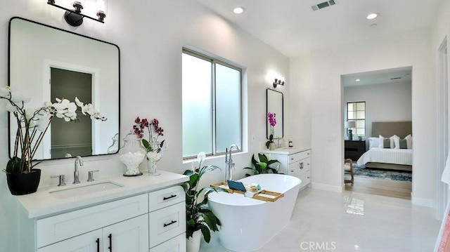 ensuite bathroom with healthy amount of natural light, a freestanding bath, recessed lighting, and two vanities