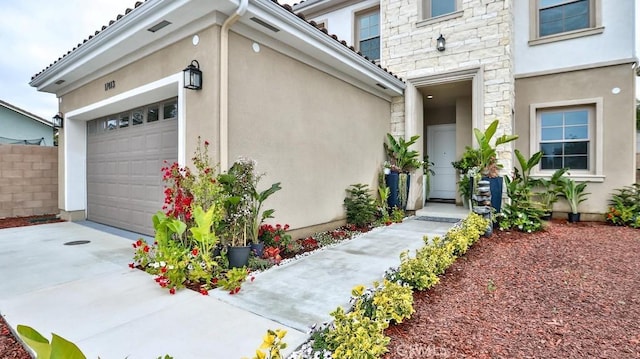 property entrance featuring stucco siding, stone siding, a garage, and concrete driveway
