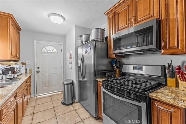 9502 Westminster Ave, Garden Grove, CA 92844 - kitchen featuring appliances with stainless steel finishes, brown cabinetry, light tile patterned flooring, and light stone countertops