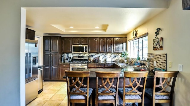 86069 Village Unit 69, Costa Mesa, CA 92626 - kitchen with appliances with stainless steel finishes, a tray ceiling, decorative backsplash, a peninsula, and dark brown cabinetry