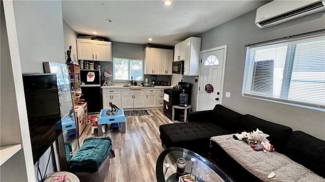 6916 Claire Ave, Reseda, CA 91335 - kitchen featuring a wall mounted AC, black appliances, light wood-style flooring, white cabinetry, and light countertops