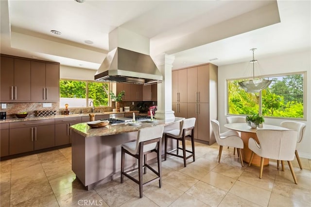 3336 Villa Mesa Rd, Pasadena, CA 91107 - kitchen featuring island exhaust hood, decorative backsplash, a breakfast bar area, light stone countertops, and decorative columns