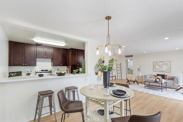 kitchen featuring stainless steel range with electric cooktop, dark brown cabinetry, light wood finished floors, light countertops, and decorative light fixtures