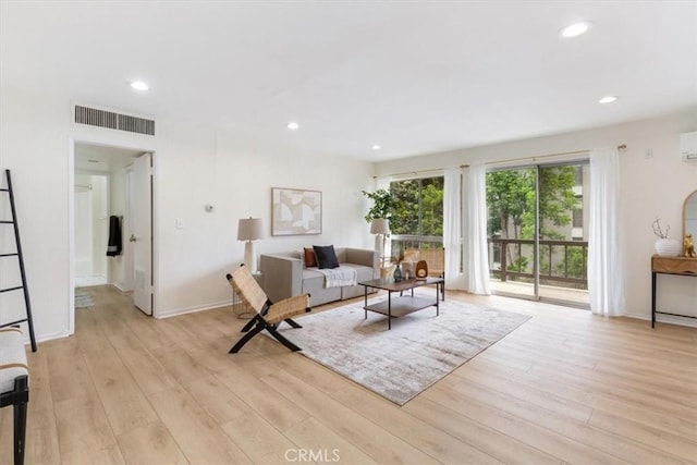 living room with light wood-style flooring, recessed lighting, a wall unit AC, and baseboards