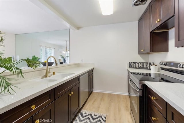 kitchen featuring appliances with stainless steel finishes, a sink, dark brown cabinets, light wood finished floors, and light stone counters