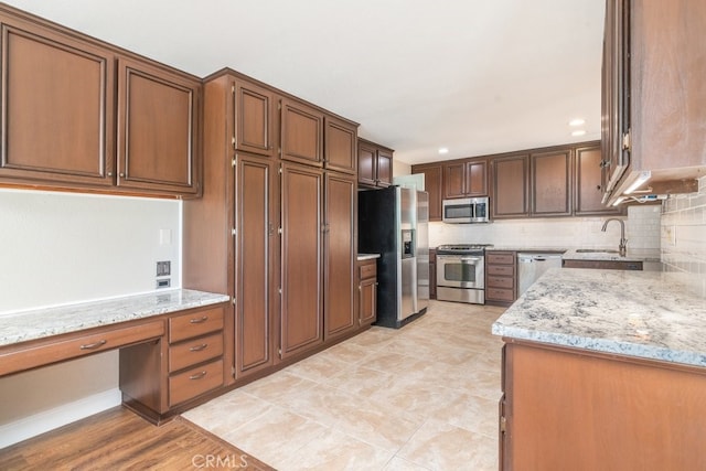 kitchen featuring stainless steel appliances, a sink, light stone countertops, and decorative backsplash