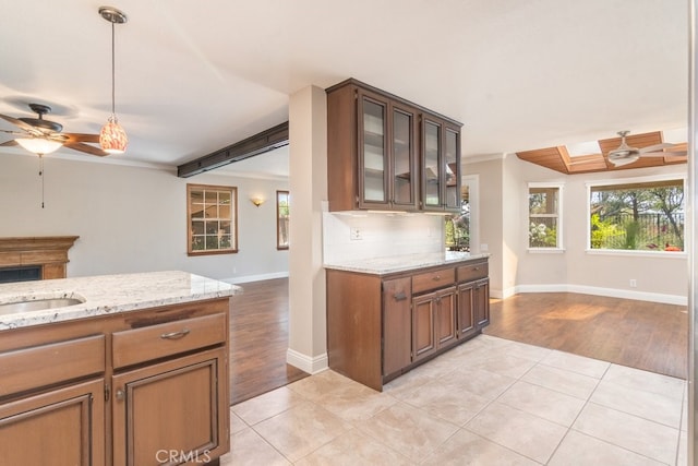kitchen with a ceiling fan, baseboards, light tile patterned floors, light stone countertops, and ornamental molding