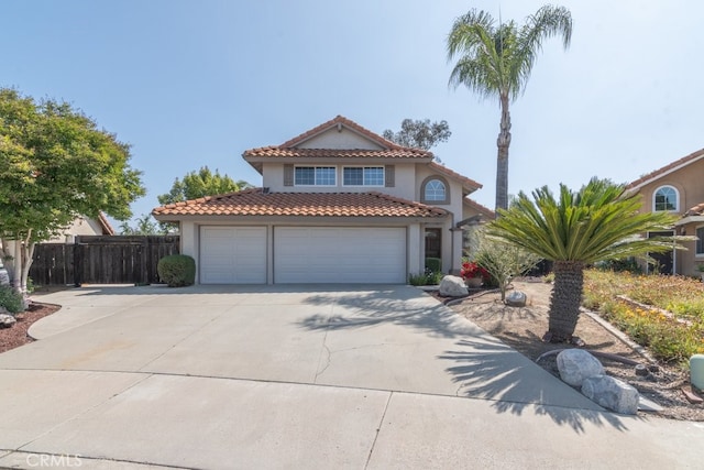 mediterranean / spanish house with stucco siding, concrete driveway, a tiled roof, fence, and an attached garage
