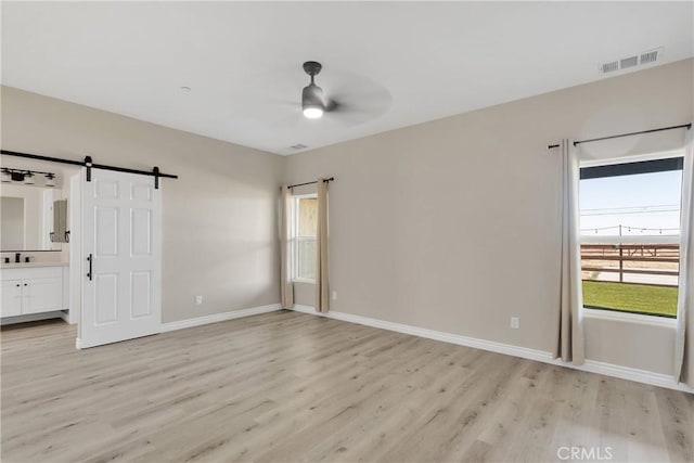 21192 Zuni Rd, Apple Valley, CA 92307 - unfurnished bedroom with light wood finished floors, a barn door, baseboards, and connected bathroom