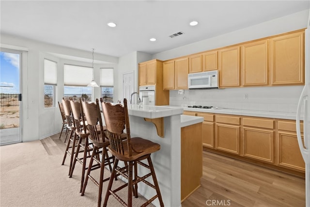 9011 Honeysuckle Ave, Hesperia, CA 92344 - kitchen featuring white appliances, tile counters, a breakfast bar area, an island with sink, and light wood-style flooring