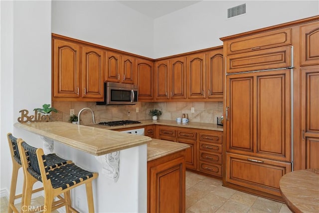 123 Costa Brava, Laguna Niguel, CA 92677 - kitchen with appliances with stainless steel finishes, tasteful backsplash, a breakfast bar, light countertops, and brown cabinetry