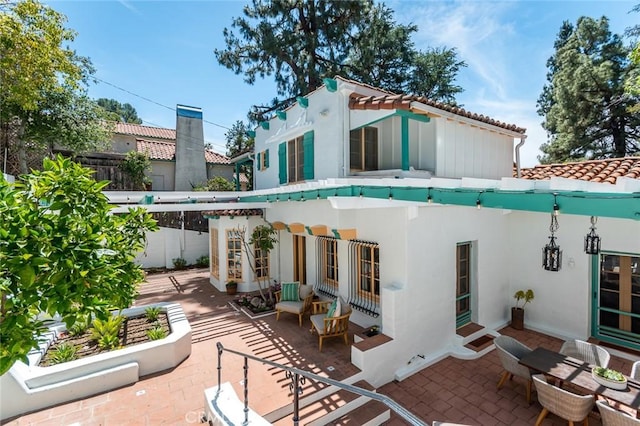 rear view of house with a tile roof, stucco siding, and a patio area