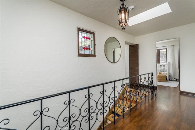 hallway featuring wood finished floors, a skylight, an upstairs landing, and baseboards