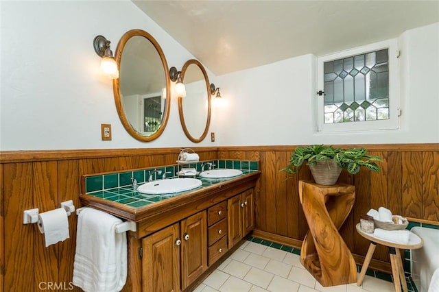 bathroom with a wainscoted wall, tile patterned floors, double vanity, and wooden walls