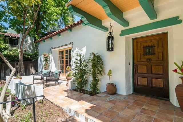 property entrance featuring stucco siding, fence, and a tiled roof