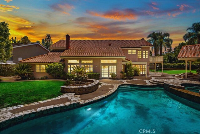 26021 Flintlock Ln, Laguna Hills, CA 92653 - back of house at dusk featuring french doors, a tiled roof, a balcony, a lawn, and a patio area