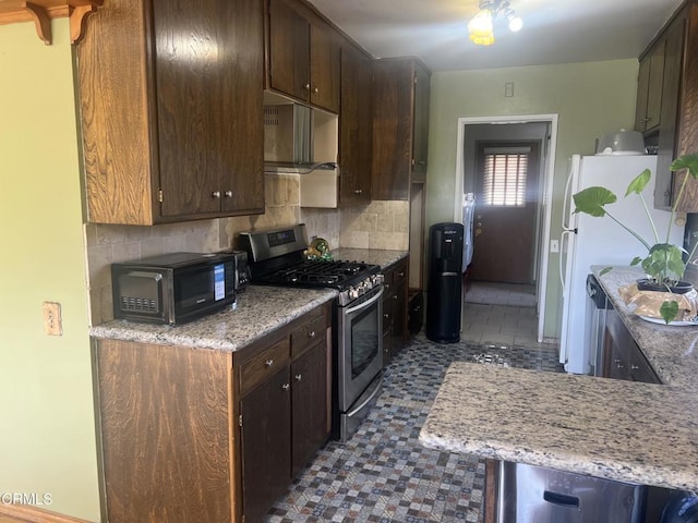 kitchen featuring stainless steel range with gas stovetop, backsplash, freestanding refrigerator, black microwave, and dark brown cabinets