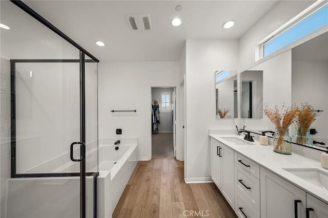 bathroom with wood finished floors, a shower stall, a bath, double vanity, and baseboards