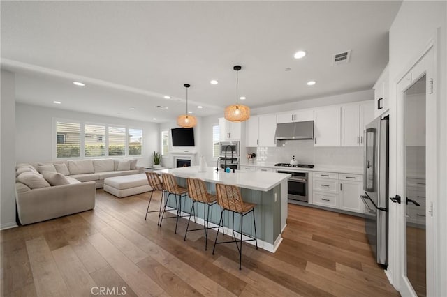 kitchen with open floor plan, stainless steel appliances, under cabinet range hood, a breakfast bar, and recessed lighting