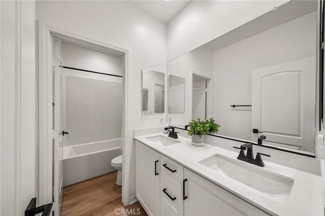 full bathroom featuring toilet, wood finished floors, double vanity, and shower / tub combination