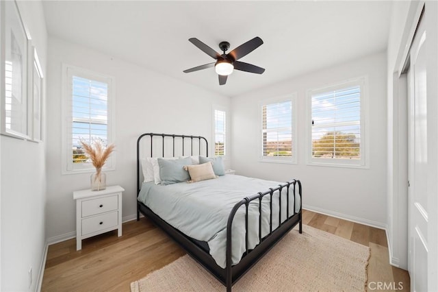 bedroom featuring multiple windows, light wood-style floors, baseboards, and a ceiling fan