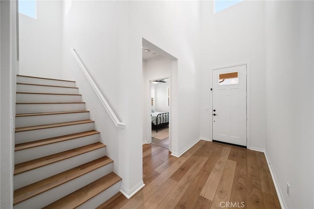 foyer entrance featuring stairs, light wood-style floors, a towering ceiling, and baseboards