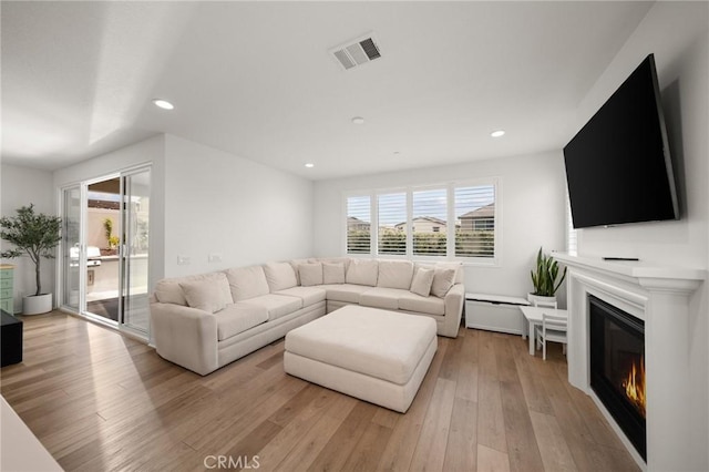 living area with a glass covered fireplace, recessed lighting, and light wood-type flooring