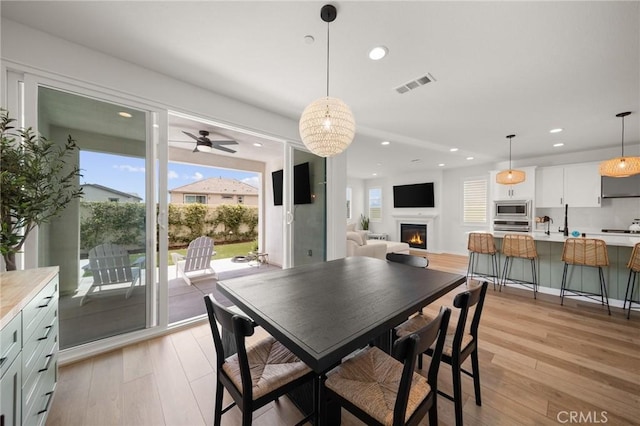 dining space with light wood finished floors, recessed lighting, a warm lit fireplace, and ceiling fan