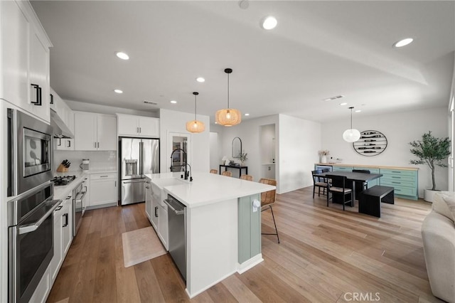 kitchen featuring appliances with stainless steel finishes, wall chimney exhaust hood, light countertops, a breakfast bar area, and recessed lighting