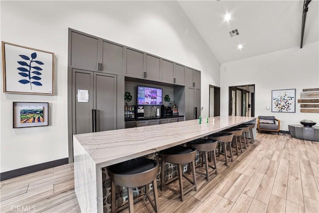 kitchen with high vaulted ceiling, light stone counters, a breakfast bar area, light wood-style flooring, and gray cabinetry
