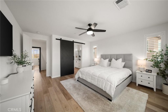 bedroom featuring a barn door, light wood finished floors, baseboards, a ceiling fan, and ensuite bathroom