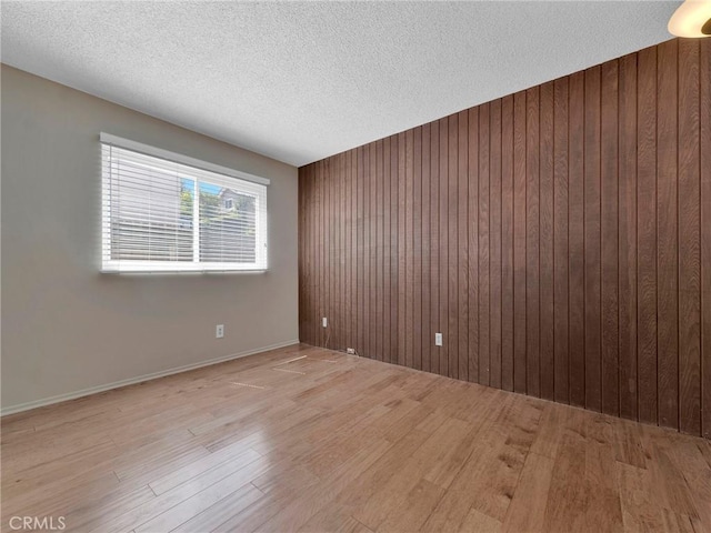 empty room featuring light wood-style flooring, wooden walls, and a textured ceiling
