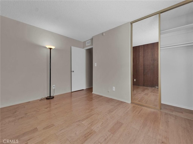 unfurnished bedroom with light wood finished floors, a closet, a textured ceiling, and baseboards