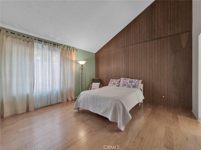 bedroom featuring lofted ceiling, light wood-type flooring, and wood walls