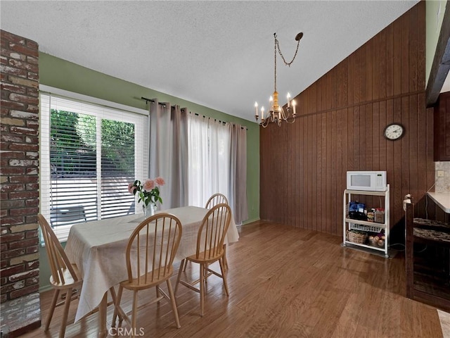 dining room with a chandelier, wood finished floors, wood walls, high vaulted ceiling, and a textured ceiling