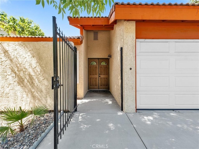 property entrance with stucco siding, a gate, a garage, and a tile roof