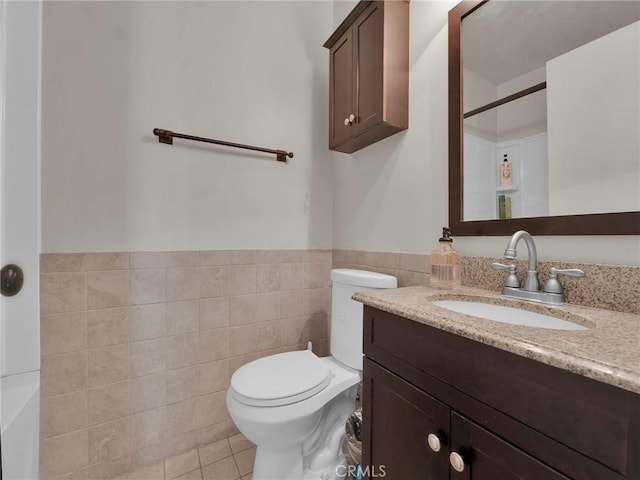 full bath featuring toilet, vanity, tile walls, tile patterned flooring, and a wainscoted wall