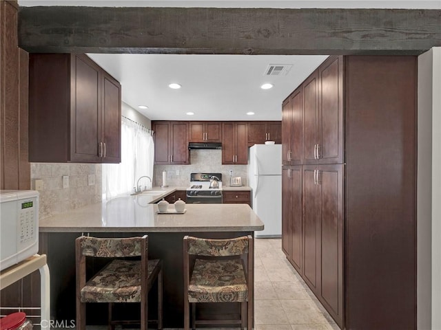 kitchen with white appliances, a sink, under cabinet range hood, a peninsula, and backsplash