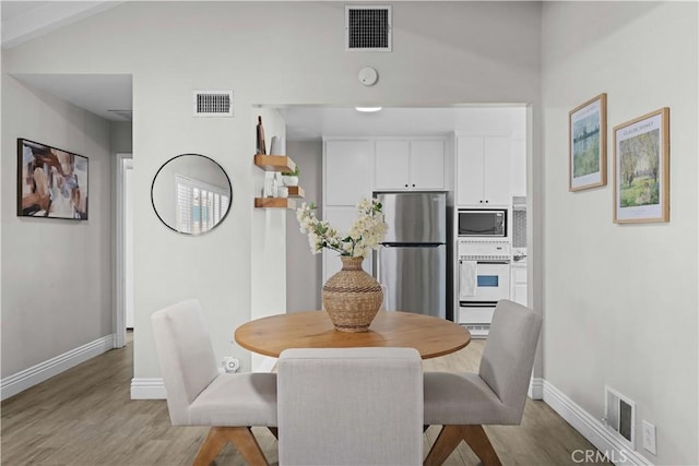 dining area featuring light wood finished floors, baseboards, and vaulted ceiling