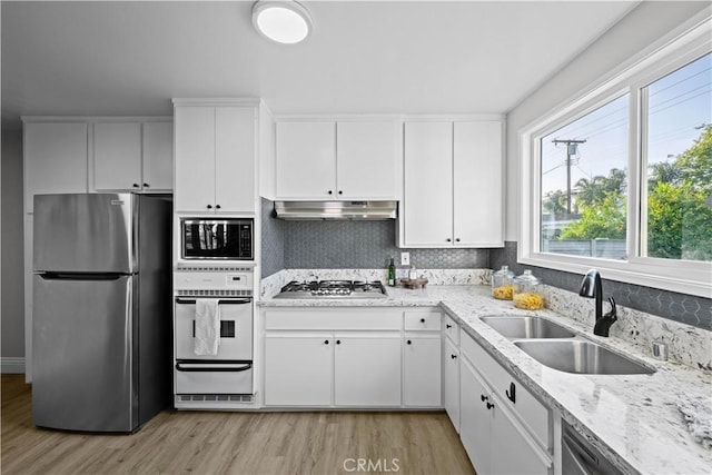 kitchen with appliances with stainless steel finishes, a sink, under cabinet range hood, light wood finished floors, and a warming drawer