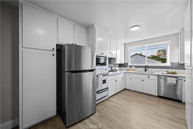 kitchen featuring appliances with stainless steel finishes, a sink, light wood finished floors, white cabinets, and backsplash