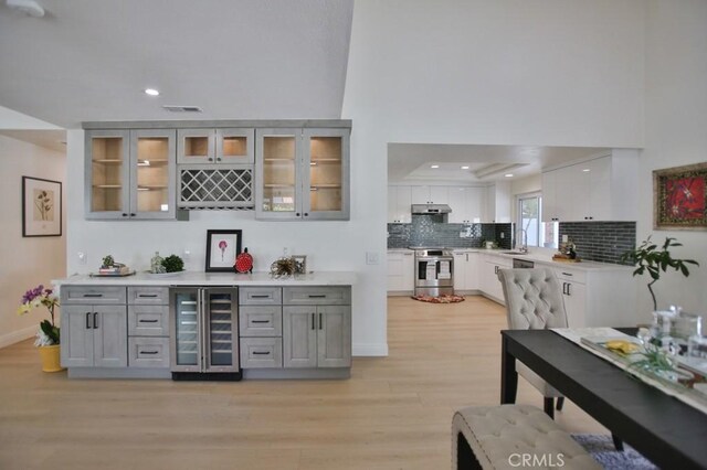 17041 Malta Cir, Huntington Beach, CA 92649 - indoor dry bar featuring beverage cooler, stainless steel electric range, under cabinet range hood, light wood finished floors, and tasteful backsplash