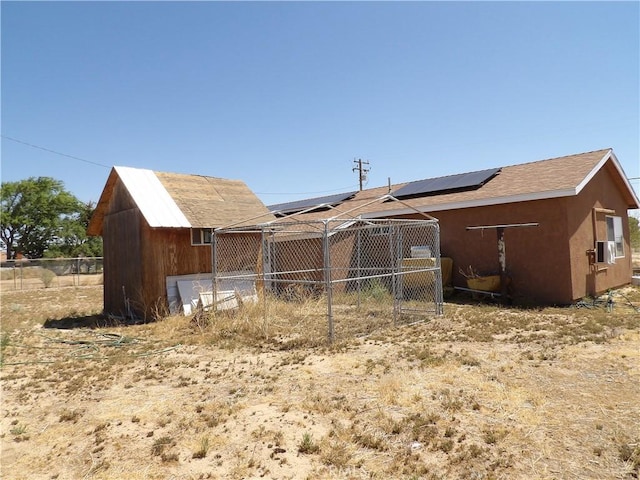 back of house featuring roof mounted solar panels, fence, and an outbuilding