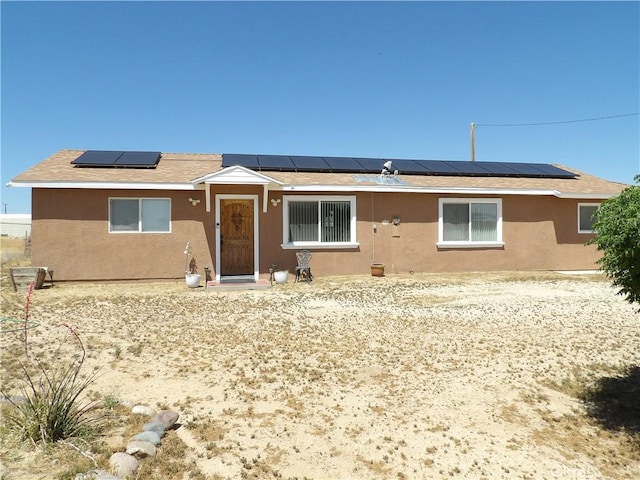 single story home with roof mounted solar panels and stucco siding