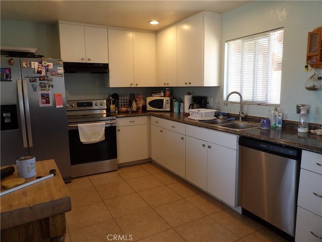 kitchen with stainless steel appliances, a sink, under cabinet range hood, dark countertops, and white cabinets