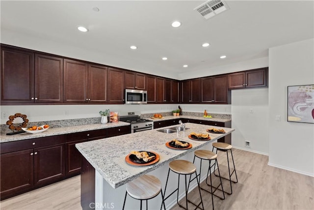 kitchen featuring appliances with stainless steel finishes, light wood-style floors, light stone counters, recessed lighting, and dark brown cabinetry