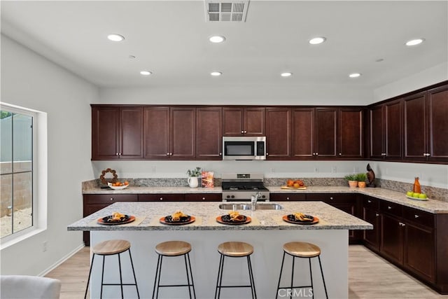 kitchen featuring appliances with stainless steel finishes, a sink, light stone countertops, light wood-type flooring, and a breakfast bar