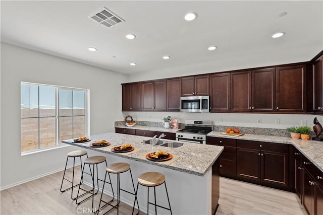 kitchen with appliances with stainless steel finishes, a sink, light wood-style flooring, a kitchen breakfast bar, and light stone counters