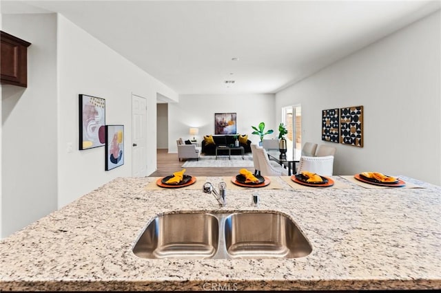 kitchen with a sink, light stone counters, wood finished floors, open floor plan, and dark brown cabinets